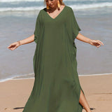 A woman wearing an elegant green V-neck caftan, a lightweight and flowy beach dress, standing on a beach near the water.