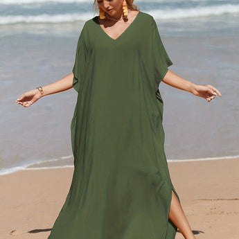 A woman wearing an elegant green V-neck caftan, a lightweight and flowy beach dress, standing on a beach near the water.