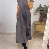 Elegant grey pleated midi dress with side cut-outs, featuring long sleeves and a fitted waist, styled with sunglasses. The dress falls to knee length and is displayed against a natural background with plants.