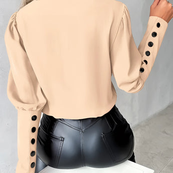 
A woman wearing an elegant light pink blouse with buttoned sleeves, showcasing the upper body and shoulders.