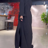 Elegant long black maxi dress with high collar and pockets worn by a fashion model; features long sleeves and a defined waist, suitable for formal events.