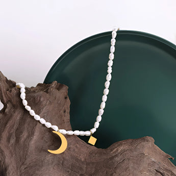 Elegant minimalist pearl choker with a gold moon pendant displayed on a wooden surface.