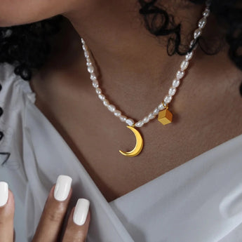 A woman's neck adorned with an elegant minimalist pearl choker featuring a gold moon pendant.
