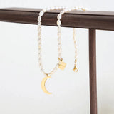 Elegant minimalist pearl choker with a gold moon pendant displayed on a wooden surface.