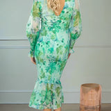 Elegant pink floral maxi dress with long sleeves worn by a model, showcasing a flowing silhouette suitable for an autumn evening. The dress features intricate floral patterns, complemented by the model's soft curls and delicate pose with visible arms and legs.