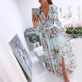 Elegant pink floral maxi dress featuring a deep V neckline, long sleeves, and a high slit. The dress is adorned with a floral pattern and styled with sunglasses, emphasizing the waist and thigh area.