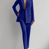 
A woman modeling an elegant blue tailored blazer and trouser set, featuring a structured shoulder and classic collar, suitable for formal or business occasions. The ensemble is designed with attention to detail, emphasizing the waist for a flattering fit.