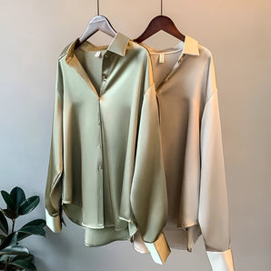 Elegant silk blouse for women hanging on a clothes hanger, featuring a luxurious satin fabric with a button-up front, tailored collar, and long sleeves, showcasing a sophisticated fashion design.