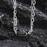 Elegant silver chain necklace with a black stone pendant displayed on a wooden surface.