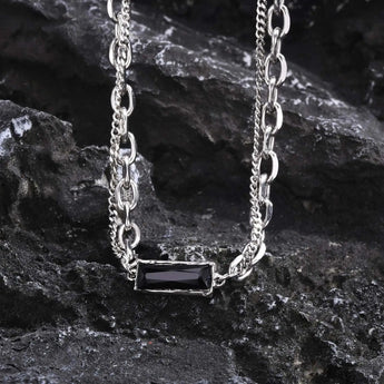 Elegant silver chain necklace with a black stone pendant displayed on a wooden surface.
