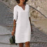 White knee-length dress with a V-neck and 3/4 sleeves, styled for a business casual look. The dress is tailored to accentuate the waist, suitable for professional settings. A Fedora hat complements the ensemble.