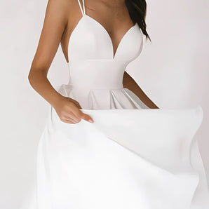 Elegant white bridal gown with a plunging neckline and spaghetti straps, featuring a flowing silhouette around the waist. The gown is worn by a woman with styled hair, with emphasis on the neckline and shoulders, captured in flash photography.