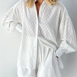 Elegant white lace blouse with sheer panels and intricate embroidery, featuring long sleeves and a stylish neckline, worn by a person.