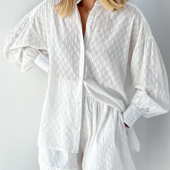 Elegant white lace blouse with sheer panels and intricate embroidery, featuring long sleeves and a stylish neckline, worn by a person.
