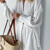 Elegant white lace blouse with sheer panels and intricate embroidery, featuring long sleeves and a structured collar.