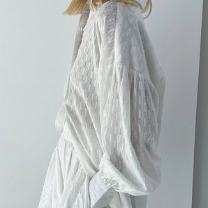 Elegant white lace blouse with sheer panels and intricate embroidery on sleeves and waist, modeled by a woman with dark hair.