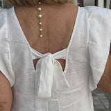 Elegant white linen V-neck summer dress displayed with a delicate pearl necklace, showcasing the dress's simple yet sophisticated design.