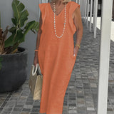 A woman wearing an elegant white linen V-neck summer dress accessorized with a pearl necklace. The dress features short sleeves and is styled with sunglasses. In the background, there is a houseplant in a flowerpot.