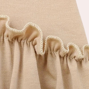 Elegant white mini dress with ruffle hem, featuring short sleeves, displayed on a wooden table with neutral-colored linens in the background.