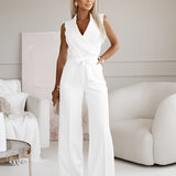 Woman modeling an elegant white sleeveless V-neck belted formal jumpsuit, showcasing the shoulder, neck, waist, and thigh areas, captured with flash photography.