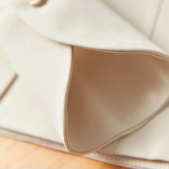 Elegant women's high-waist trouser suit and pleated blouse set in beige, displayed on a comfortable couch.