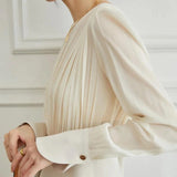 Elegant women's high-waist trouser suit and pleated blouse set in beige, featuring tailored outerwear, a structured shoulder design, long sleeves, and a defined waist, styled with a dress shirt neckline.