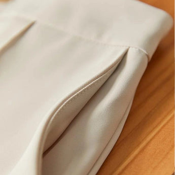 Elegant women's high-waist trouser suit and pleated blouse set in beige, featuring a blazer with a notch collar and button closure, paired with a dress shirt-style blouse with long sleeves.