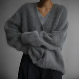 Elegant women's oversized sweater made of soft fur material in a plush, woolen texture, featuring long sleeves, a high collar, and a grey color. The sweater is shown wrapped around a model, highlighting its cozy and fashionable winter design.