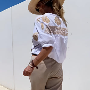 Embroidered boho loose fit blouse in a summer fashion chic style, featuring intricate embroidery, loose sleeves, and a comfortable fit. The blouse is worn by a model accessorized with a stylish hat, sunglasses, and a handbag, highlighting the blouse's bohemian aesthetic.