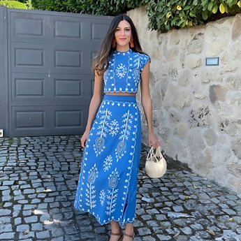 Embroidered white linen sleeveless midi dress displayed against a light background, showcasing the dress's azure embroidery detail and fitted waist design.