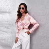 Elegant woman wearing an emerald green satin long sleeve button-down blouse, with sunglasses perched on her head, showcasing the smooth and lustrous material and stylish design.
