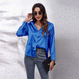 Emerald green satin long sleeve button-down blouse with a smooth finish, featuring a buttoned-up collar and loose-fitting sleeves, worn by a person with sunglasses.