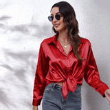 
A person wearing an emerald green satin long sleeve button-down blouse, showcasing the blouse's elegant sheen and button detailing.