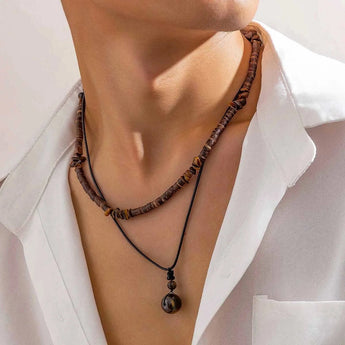 A person's hand adjusting a bohemian ethnic tribal wooden bead necklace worn around the neck, paired with a colorful dress.