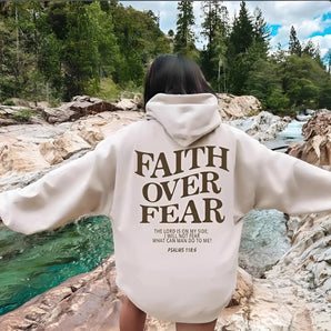 A person wearing a "Faith Over Fear" hoodie with a Christian Psalms 118:6 inspirational message, standing outdoors with trees and sky in the background.