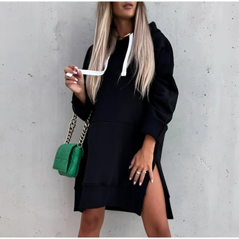 Woman wearing an olive green cap, beige trench coat, knit dress, and sock boots, holding a chain handbag.