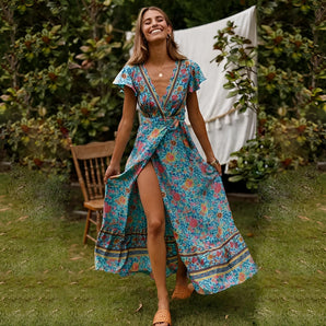 Woman wearing a floral blue boho maxi dress with a high slit and V-neck, posing outdoors with a smile, showcasing the lightweight summer fabric and fashionable design.