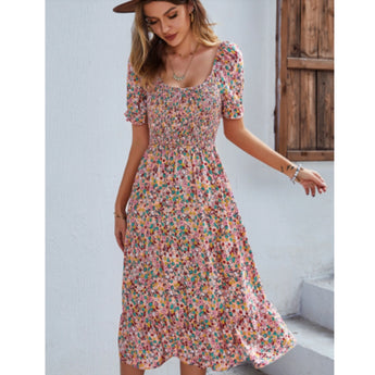 Woman wearing a pink floral boho maxi dress with puff sleeves and a high slit, styled with a fashionable hairstyle and a hat.