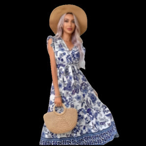 Blue and white boho floral maxi dress with a V-neck design, featuring short sleeves and a fitted waist. The dress is styled for a summer beach look, suitable for daytime wear. The model is wearing a hat and showcasing the dress in a Royal Blue shade, size 2XL.