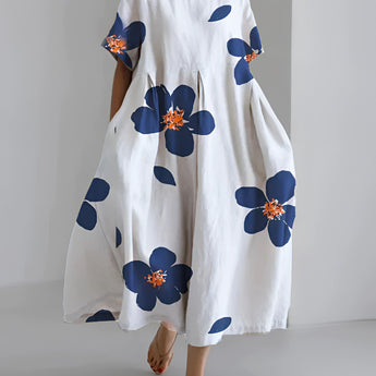 White floral maxi dress in an oversized print, featuring a unique contemporary design, suitable for plus size 5XL. The dress has sleeves and a neckline, and is designed for daytime wear.