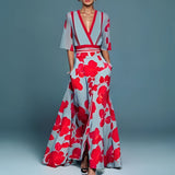 Floral maxi dress featuring a red poppy print, designed with a V-neck, belted waist, and high slit, modeled by a fashion model.