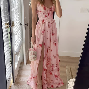 Pink floral maxi dress with a slit, featuring short sleeves and a fitted waist, suitable for a summer garden party, modeled by a person standing near a door.