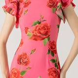 Pink floral mermaid dress with ruffle details, featuring a fitted waist and elegant sleeves, suitable for garden parties. The dress is adorned with floral patterns, complementing a lush green and flower-filled background.