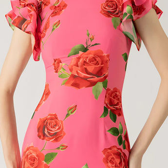 Pink floral mermaid dress with ruffle details, featuring a fitted waist and elegant sleeves, suitable for garden parties. The dress is adorned with floral patterns, complementing a lush green and flower-filled background.
