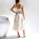 Floral midi dress in pastel colors with a garden party print, featuring short sleeves and a fitted waist, perfect for vacation or sundress occasions. The model is standing, showcasing the dress's elegant design and flowing fabric.