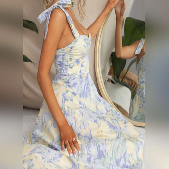 Floral midi dress in a pastel garden party design, featuring a blue color scheme. The dress is styled for vacation wear with comfortable short sleeves and a fitted waist, falling to a midi length around the thighs. The model is wearing an XL size, showcasing a stylish and fashionable one-piece garment.