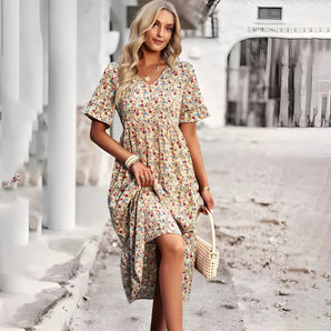 Floral print short sleeve asymmetrical summer dress in apricot, shown in XL size. The dress features a chic and lightweight design with an elegant waistline, and is worn by a standing model with stylish eyewear.