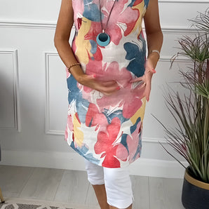 Woman wearing a floral print sleeveless summer tunic top with various flowers and leaves in the design, showcasing the shoulder and neck area against a plain white background.