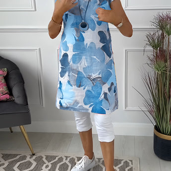 A woman wearing a sleeveless summer tunic top with a floral print design in shades of blue and white, featuring a round neckline and a relaxed fit at the waist.