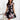 A woman wearing a black, floral print, sleeveless summer dress that is lightweight and knee-length, smiling and posing.